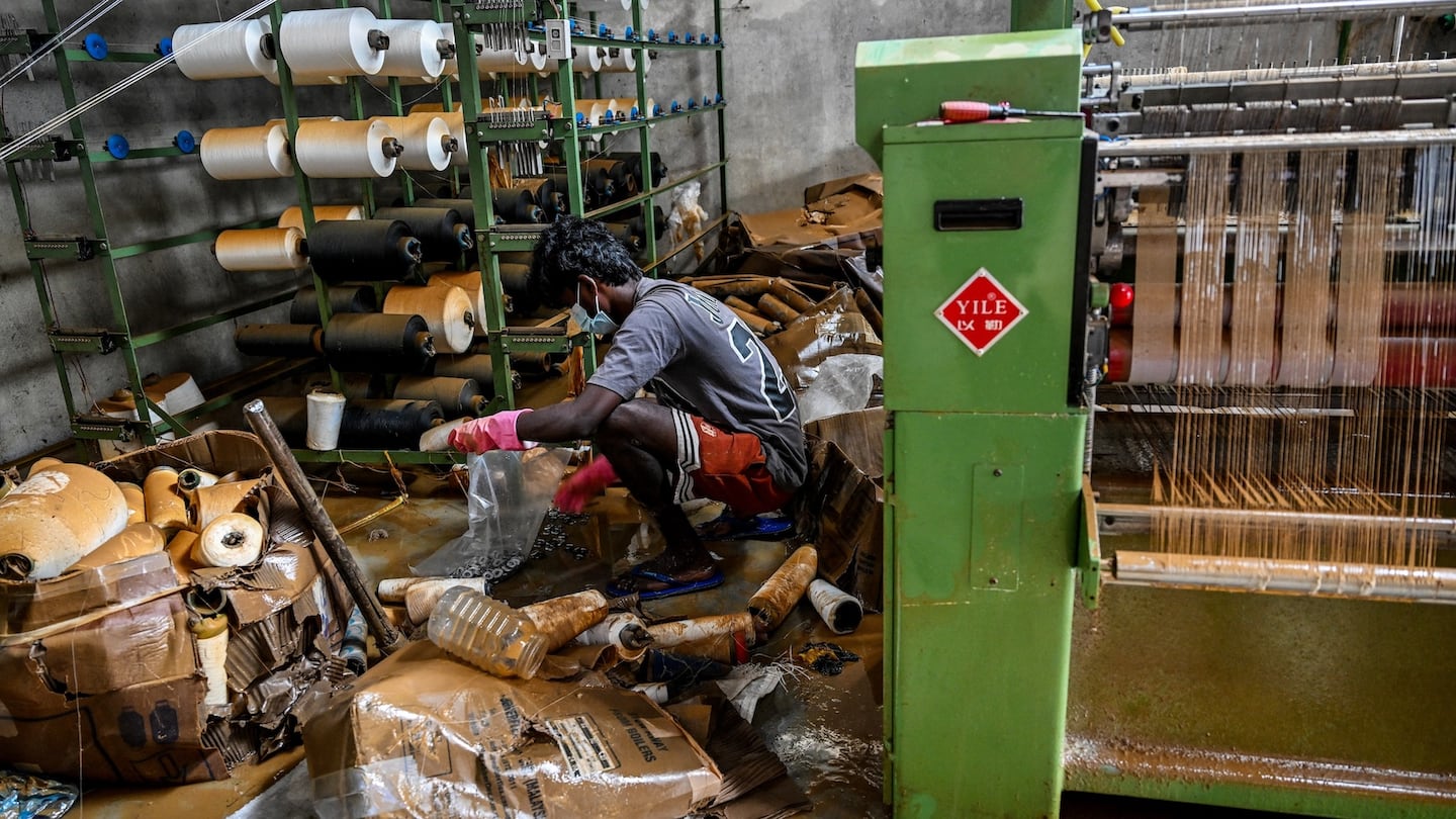 A man salvages raw materials next to a power loom at an inundated factory following flash floods in the aftermath of Cyclone Ditwah
