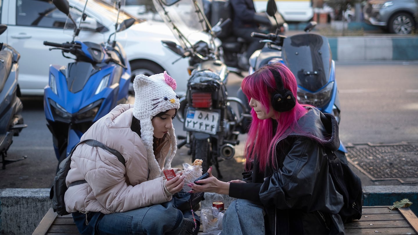 Two young Iranian women sit on the pavement in northern Tehran on December 31, 2025, following street protests across Iran.