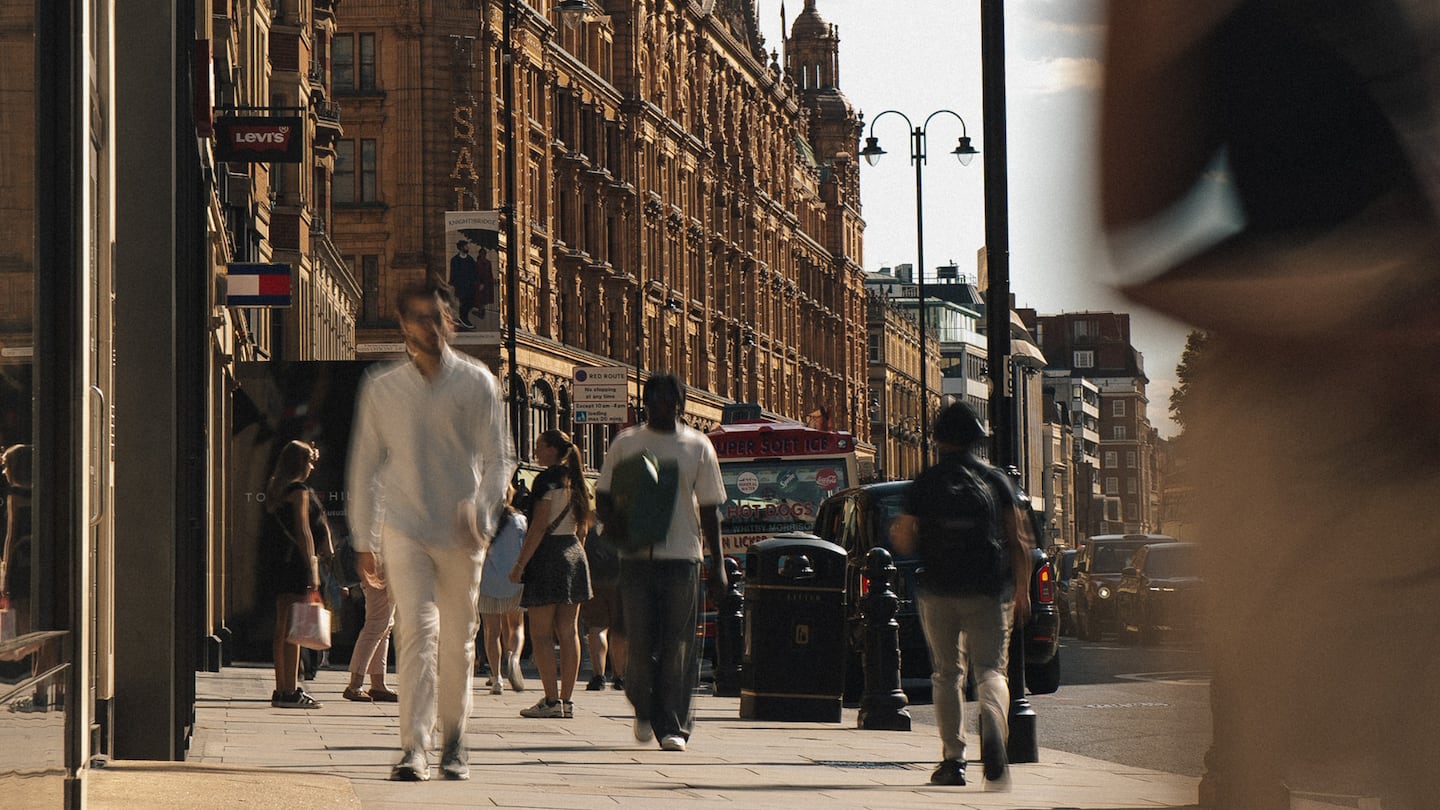 Shoppers walk down a street in London's Knightsbridge district, with department store Harrods visible behind them.