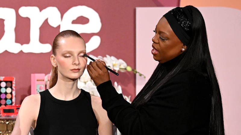 Pat McGrath applies eyeshadow with a brush to a model's face at an Allure beauty event. Both are wearing black.
