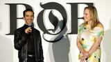 Imran Amed, founder and CEO of The Business of Fashion, with a microphone in hand and Ali Goldstein, president of US mergers and acquisitions at L'Oreal Groupe, stand before a white wall with a large BoF logo.